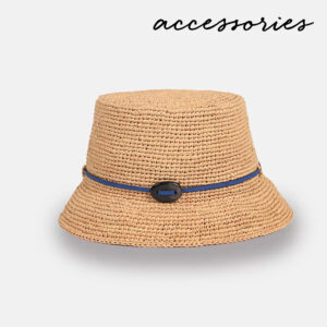 A tan woven bucket hat with a blue ribbon and black oval accent around the crown, displayed on a light gray background with the word "accessories" written in black script at the top right. Fearrington Village