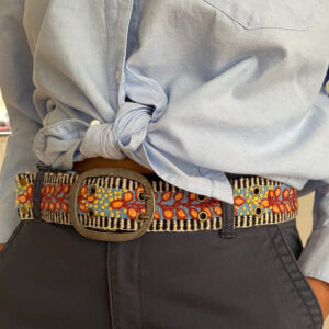 A person wearing a light blue button-up shirt tied at the waist, dark pants, and a colorful embroidered belt with a large metal buckle and vibrant patterns. Fearrington Village
