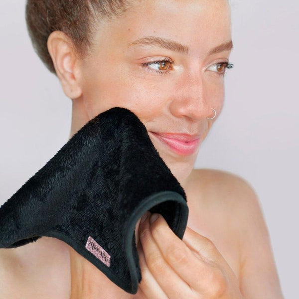 The Spa Edit - Refresh & Glow: Start Your Day with a Clean, Radiant Face 3 A person with a nose ring smiles gently while using a soft black cloth to cleanse their face. The background is plain and light, highlighting their clear skin and natural look. Fearrington Village