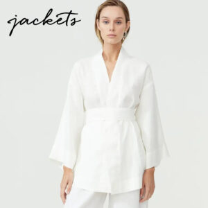 A woman wearing a white, loose-fitting jacket with wide sleeves and a belted waist, standing against a plain background. The word "jackets" is written in black script in the upper left corner. Fearrington Village