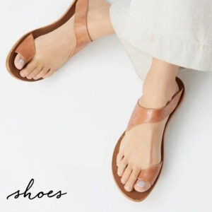 A person wearing light-colored pants and stylish tan leather sandals with a unique crisscross strap design. The word "shoes" is written in cursive in the bottom left corner. Fearrington Village