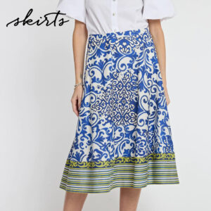 Woman wearing a white blouse and a knee-length, blue and white patterned skirt with green and yellow striped trim at the hem. The word "skirts" is written in cursive at the top left corner. Fearrington Village