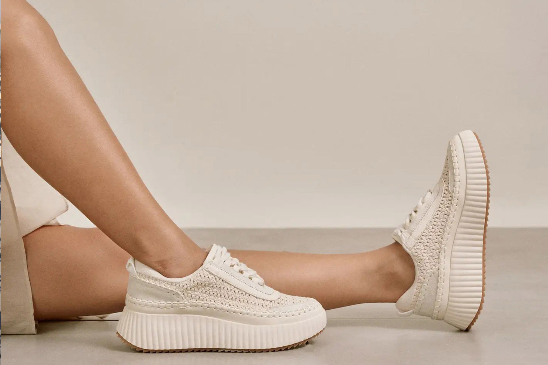 A person wearing cream-colored platform sneakers with textured detailing and thick, ridged soles sits with legs extended on a neutral background. Fearrington Village