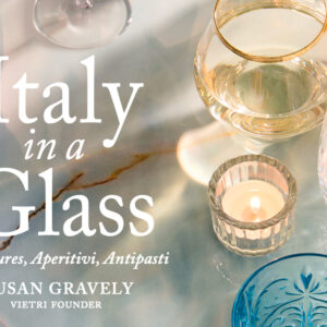 A marble table with various glasses, a candle, and a mint garnish. Text reads: "Italy in a Glass: Adventures, Aperitivi, Antipasti. Susan Gravely, Vietri Founder. Fearrington Village