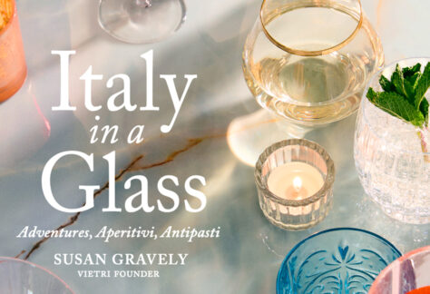 A marble table with various glasses, a candle, and a mint garnish. Text reads: "Italy in a Glass: Adventures, Aperitivi, Antipasti. Susan Gravely, Vietri Founder. Fearrington Village