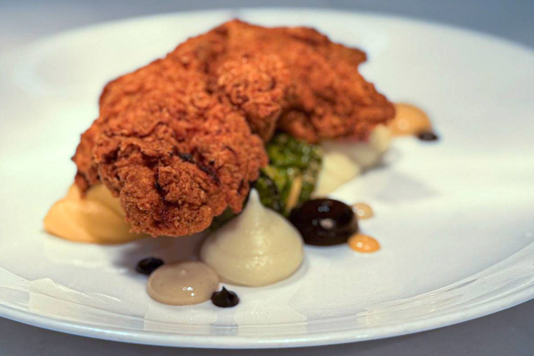 The Fearrington Plate - August 7, 2025 1 A plated dish featuring two pieces of crispy fried chicken atop vegetable purée, with dollops of assorted sauces and garnishes, served on a white plate. Fearrington Village