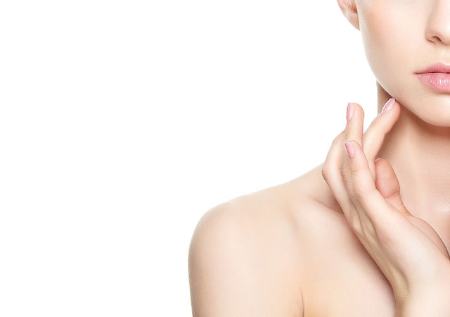 Close-up of a woman's lower face, neck, and shoulder with clear skin, touching her cheek gently with her fingers against a white background. Fearrington Village