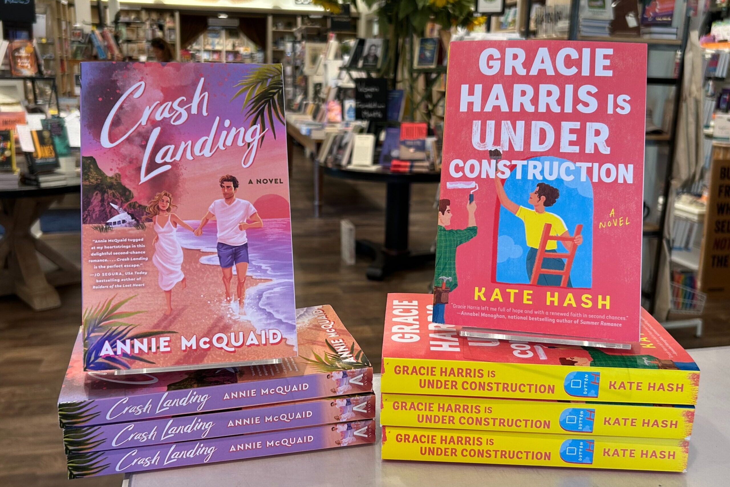 Two stacks of books are displayed in a bookstore. On the left is "Crash Landing" by Annie McQuaid with a beach scene cover; on the right is "Gracie Harris Is Under Construction" by Kate Hash with a bright, illustrated cover. Fearrington Village