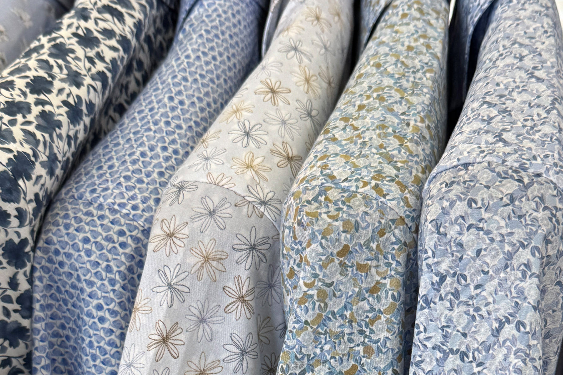 Close-up of several shirts with various blue and grey floral and geometric patterns hanging on a rack. Fearrington Village