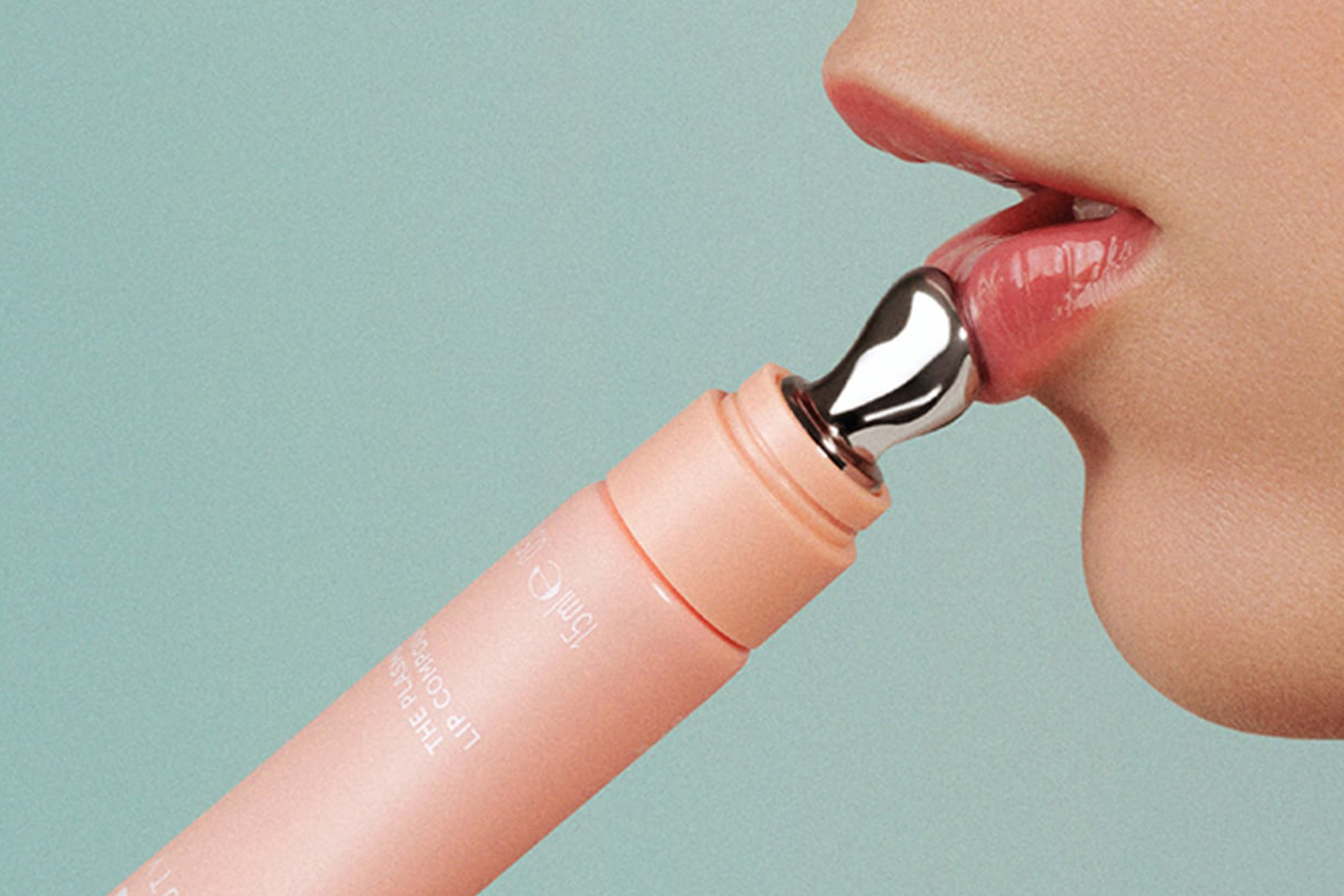 Close-up of a person applying a pink lip care product with a metallic applicator to their lips against a light blue background. Fearrington Village