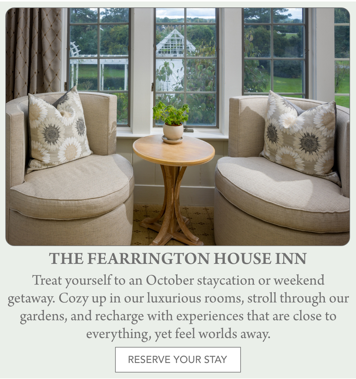 Two beige armchairs with floral pillows face each other beside a round wooden table with a potted plant, set near a window overlooking a garden. Text below invites guests to stay at The Fearrington House Inn. "Treat yourself to an October staycation or weekend getaway. Cozy up in our luxurious rooms, stroll through our gardens, and recharge with experiences that are close to everything, yet feel worlds away." Fearrington Village