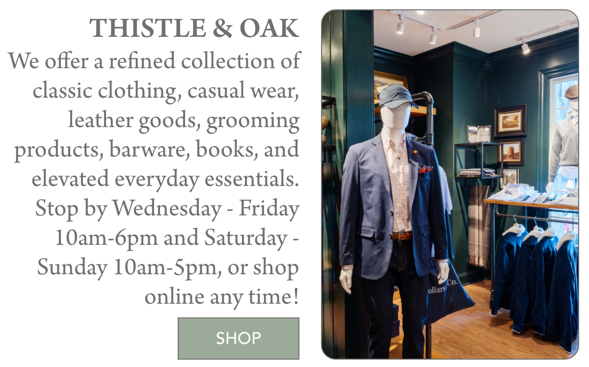 A stylish men’s clothing store display features a mannequin in a blue suit, shirt, and cap. A sign beside it invites shoppers to visit Thistle & Oak for classic clothing and gifts, with store hours and a green "Shop" button. "We offer a refined collection of classic clothing, casual wear, leather goods, grooming products, barware, books, and elevated everyday essentials. Stop by Wednesday - Friday 10am-6pm and Saturday - Sunday 10am-5pm, or shop online any time!" Fearrington Village