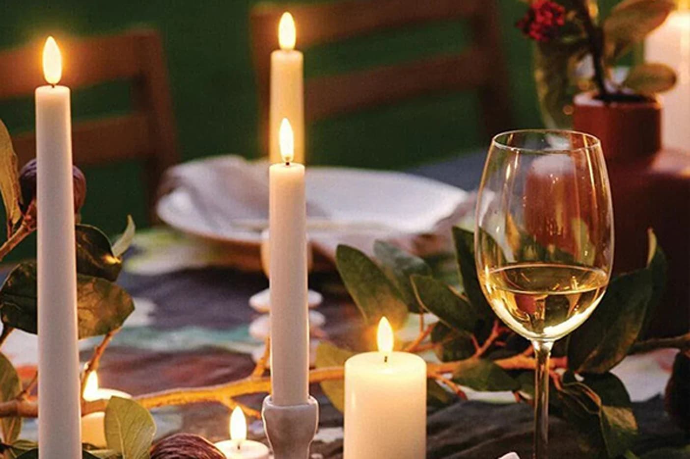 A warmly lit dinner table set with burning candles, a glass of white wine, plates, and greenery as part of the centerpiece, creating a cozy, inviting atmosphere. Fearrington Village