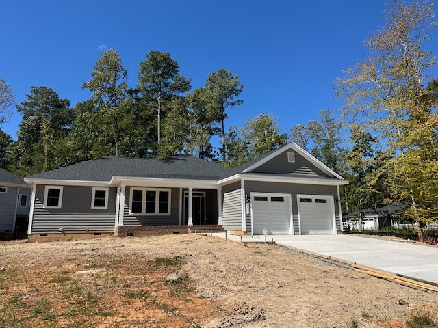 Single-story gray house with white trim, attached double garage, covered front porch, and unfinished landscaping. Surrounded by tall trees under a clear blue sky. Concrete driveway leads up to the garage. Fearrington Village
