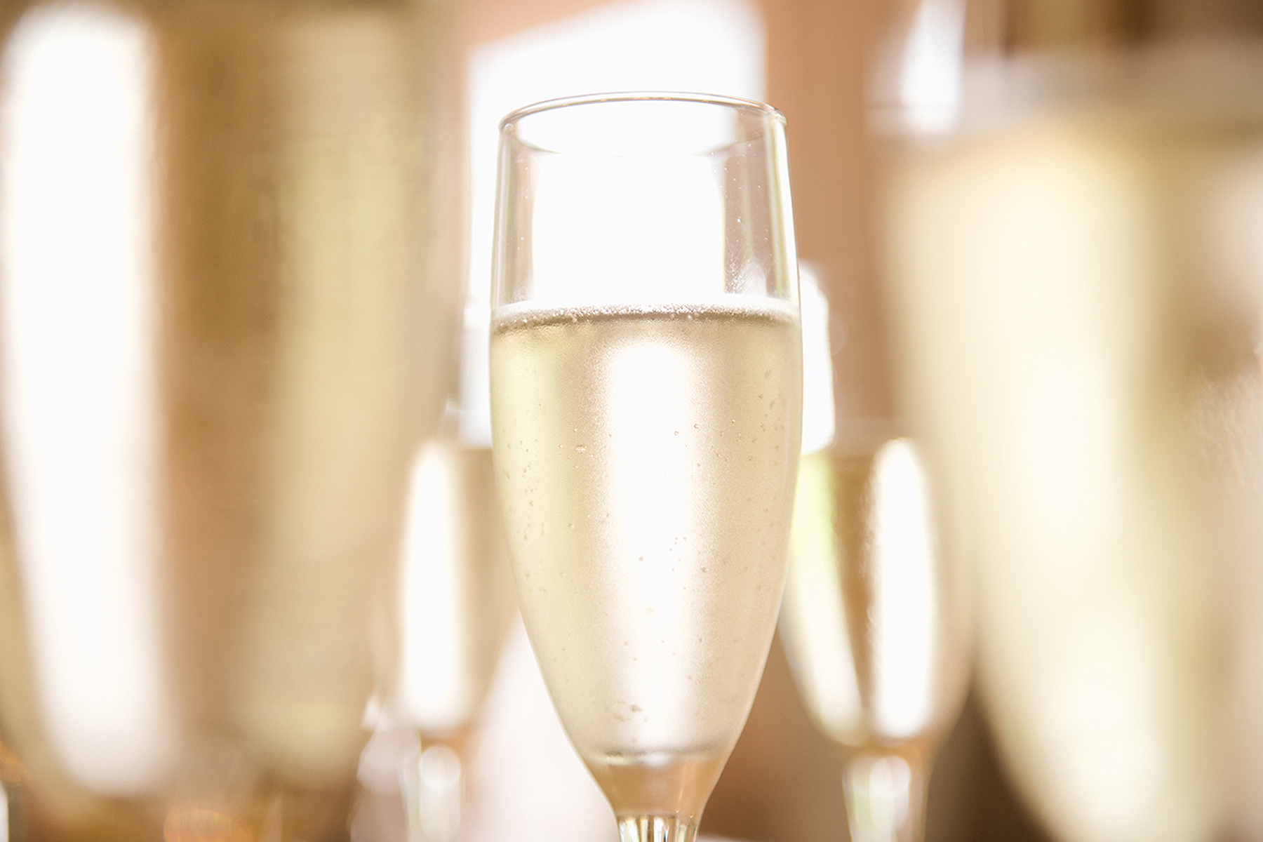 A close-up of a clear champagne flute filled with sparkling wine, surrounded by several other blurred glasses. The light background creates a celebratory and elegant atmosphere. Fearrington Village