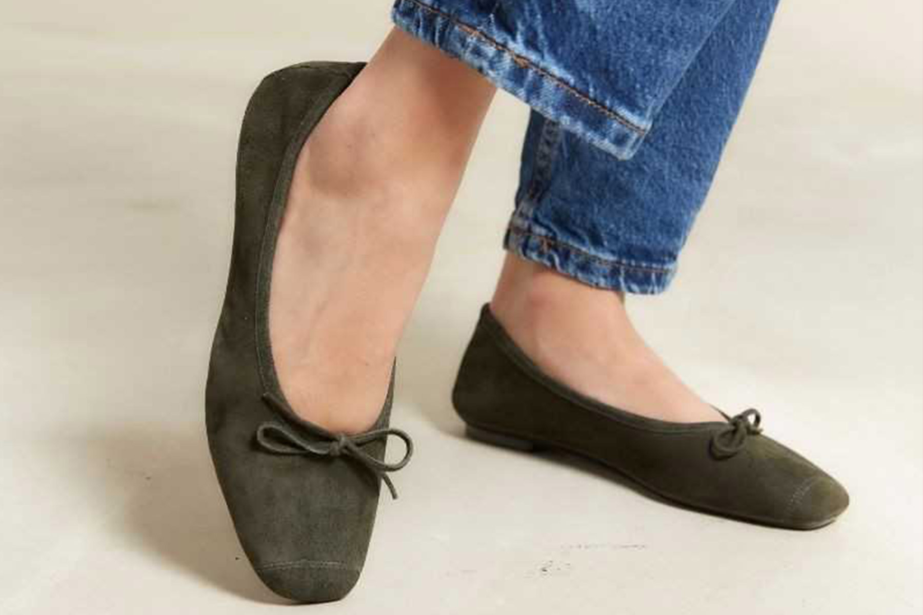 The Fearrington InnSider - Fresh Fall Finds: From France to Italy, Straight to Dovecote 1 A person wearing dark green suede ballet flats with a bow detail, paired with blue jeans, stands on a light-colored floor. Fearrington Village