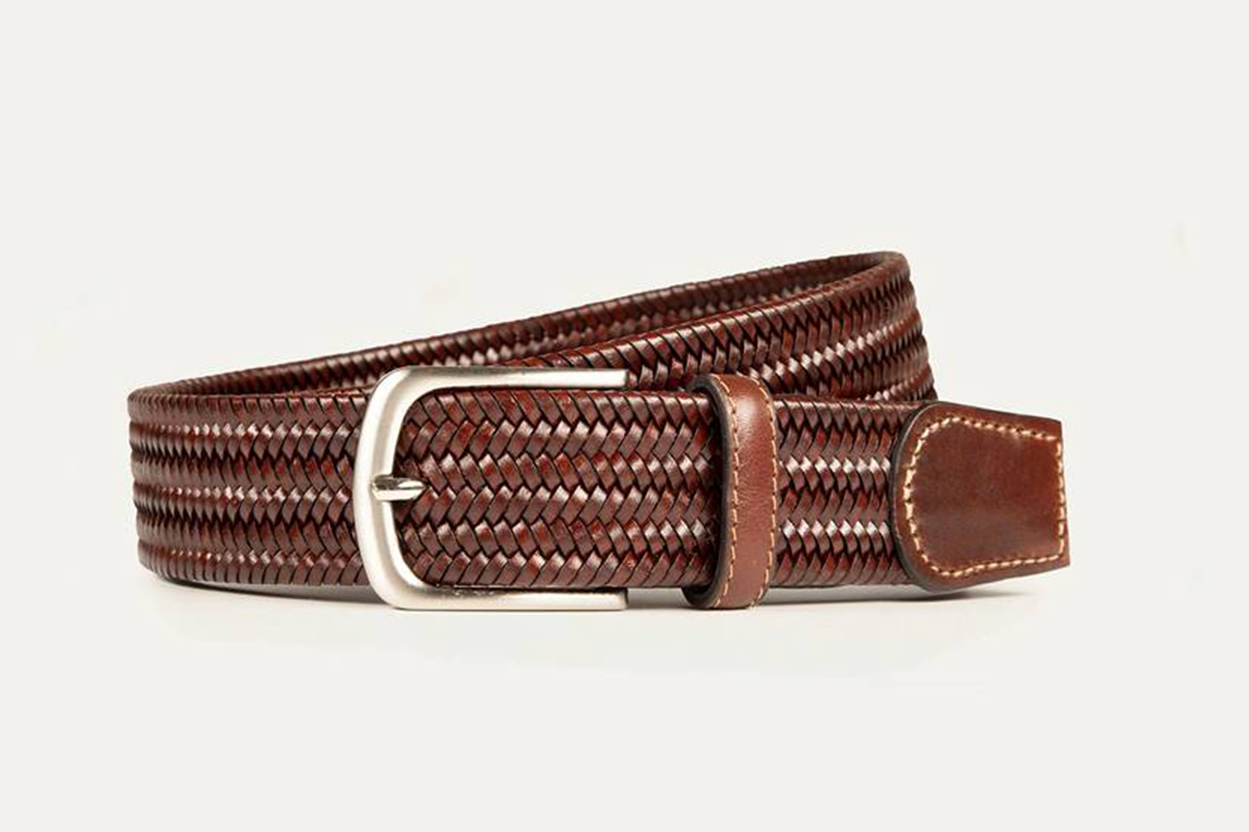 A brown woven leather belt with a silver buckle, featuring light stitching on the leather end and belt loop, displayed against a plain white background. Fearrington Village