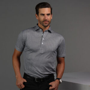 Thistle & Oak Gentleman's Dispatch - Collars & Co. Trunk Show — One Day Only This Friday 3 A man with short brown hair and a beard wears a short-sleeved, patterned polo shirt and black pants, standing against a plain gray background with one hand in his pocket. Fearrington Village